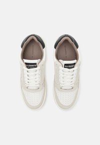 Weiße und beige Sneakers mit perforierten Details, einer schwarzen Fersenkappe und kontrastierenden Schnürsenkeln. Markenlabel auf der Zunge sichtbar.