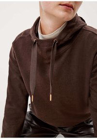 Brun hoodie tillverkad av mjukt tyg, med hög krage, dragsko med bronserade detaljer och en avslappnad passform. Stylen är slät och har en minimalistisk design.