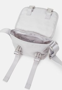 Grå nylon crossover taske med flaplukning, to grå spænder og justerbare stropper. Indvendigt har den en lille lomme og et mærke.