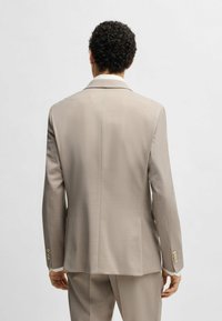Giacca da abito beige su misura con revers a punta, spacco posteriore singolo e bottoni dorati sui polsi. Tessuto liscio, design slim fit.