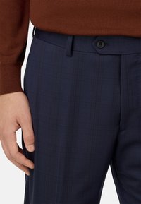 Pantalones formales azul marino hechos de tejido texturizado, con un sutil patrón de cuadros, cierre de un solo botón y bolsillos laterales.