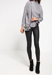 Maglione grigio a maniche lunghe e collo alto abbinato a leggings neri in ecopelle e stivaletti neri. Accessoriato con una borsa a tracolla argentata.
