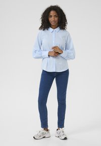 Ljusblå skjorta med krage, långa puffärmar; ihopparad med mörkblå jeans och vita sneakers med grå detaljer.