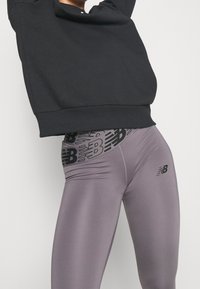 Czarna bluza z kapturem i dopasowane jasnoszare legginsy z czarnym abstrakcyjnym wzorem logo w talii i z boku.