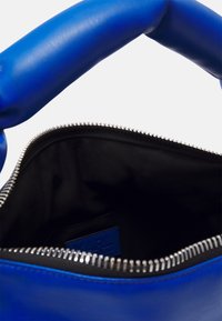 Borsa a mano in pelle blu con un manico spesso e texturizzato, apertura con cerniera argentata e interno in tessuto nero con un'etichetta di marca.