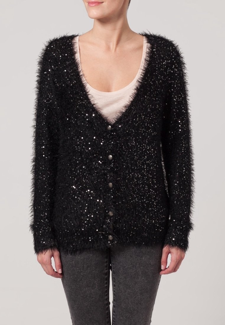 Svart fluffig cardigan med paljetter, v-ringad design, knappstängning, långa ärmar och textilstruktur. Bärs över en beige topp.
