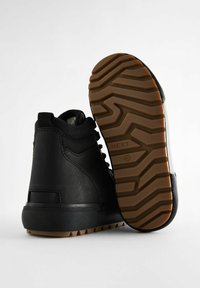 Czarne trampki typu high-top z gumową podeszwą, teksturowanym czarnym cholewką i brązowym wzorem zygzakowatym na podeszwie. Posiadają wiązanie i pętelkę na pięcie.