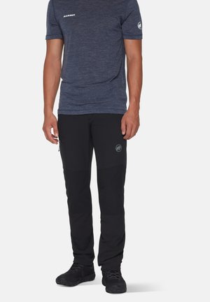 Marineblaues Kurzarmhemd mit grauem Logo, kombiniert mit schwarzen Hosen mit Knieflicken und Seitentaschen. Strukturierter, sportlicher Stil.