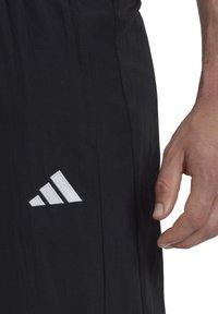 Schwarze Sportshorts mit glatter Textur, die ein weißes, gesticktes Adidas-Logo auf der linken Seite und eine Seitennahtdetails aufweisen.