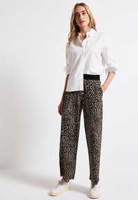 White button-up shirt with rolled sleeves, paired with loose-fit leopard print trousers and white sneakers. Trousers feature a black waistband.