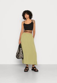 Top cropped preto com alças finas, saia maxi verde, sandálias pretas com fivela e uma mala texturizada em preto e creme. Materiais suaves e corte descontraído.