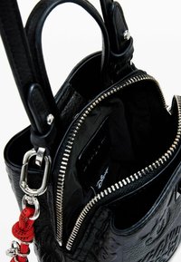 Borsa a tracolla in pelle nera con chiusura a zip, esterno texturizzato, ferramenta argento e un charm decorativo rosso. Interno foderato in tessuto nero.