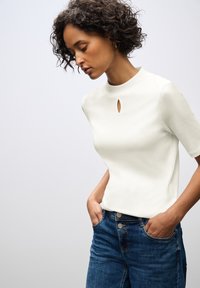Top bianco a maniche corte con scollo a chiave, abbinato a jeans in denim blu. Tessuto liscio e vestibilità comoda.