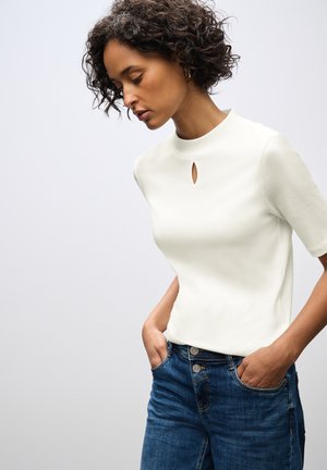 Top blanco de manga corta con escote en forma de llave, combinado con jeans de mezclilla azul. Textura de tela suave y corte relajado.