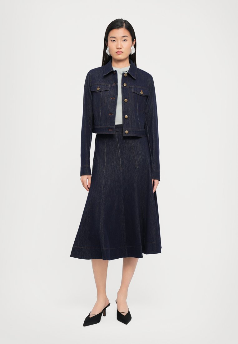 Veste en denim foncé cropped avec des boutons dorés assortis à une jupe longue. Texture lisse, design minimaliste et silhouette ajustée.