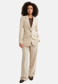 Lys beige skræddersyet jakkesæt med en enkeltknaps blazer med to knapper, pigede revers og matchende brede bukser.