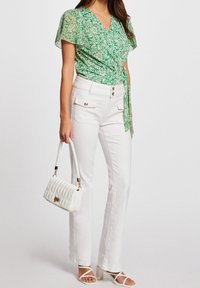 Blusa floreale verde a portafoglio con maniche corte, abbinata a jeans bianchi a vita alta con fondo svasato. Accessoriata con una borsa bianca trapuntata.