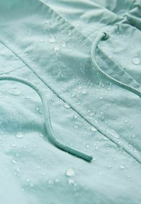 Chaqueta azul claro repelente al agua con gotas sobre el material, con cordón ajustable y tela texturizada con acabado suave.