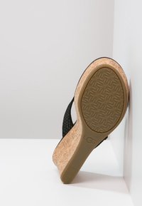 Klínové sandály s černým pleteným svrškem a korkovou mezipodešví. Obsahují texturovanou gumovou podrážku s geometrickým vzorem a značkovým logem.