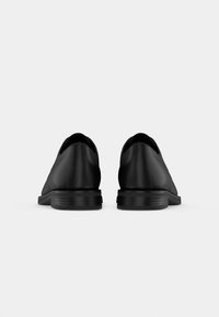 Chaussures en cuir noir au design épuré, à bout arrondi et semelle en caoutchouc texturée. L'arrière présente une finition lisse sans couture visible.
