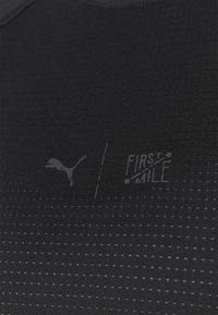 Svart atletisk topp gjord av texturerat tyg, med ett subtilt rutmönster och logotyper för Puma och "First Mile" i en något ljusare nyans.