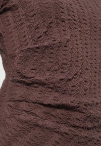 Καφέ υφασμάτινη υφή με γεωμετρικό μοτίβο, με απαλή και ελαφρώς ζαρωμένη επιφάνεια. Ο σχεδιασμός περιλαμβάνει υφαντά στοιχεία και διακριτικό βάθος.