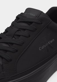 Μαύρο χαμηλό αθλητικό παπούτσι Calvin Klein με μαύρα κορδόνια και διακριτικό λογότυπο CK χαραγμένο στο πλάι και στη γλώσσα.