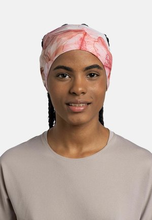 Joven con el cabello trenzado que lleva una diadema floral rosa claro y una camiseta beige, mirando hacia adelante con una ligera sonrisa.