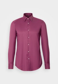 Chemise habillée homme à manches longues de couleur prune unie avec col pointu et boutons blancs sur le devant sur un fond clair.