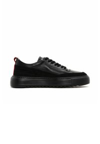 Baskets en cuir noir avec des surfaces lisses et texturées, ornées d'un accent rouge sur le talon et d'une semelle en caoutchouc épaisse.