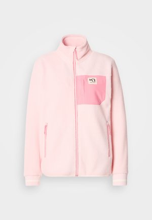 Gaiši rozā vilnas jaka ar rāvējslēdzēju priekšpusē, augstu apkakli un kontrastējošu rozā krūšu kabatu ar logotipu. Ir sānu kabatas ar rāvējslēdzējiem.