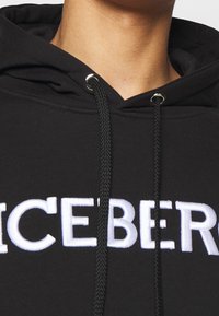 Sudadera negra con capucha y cordones, con herrajes plateados, adornada con un atrevido texto blanco bordado que dice "ICEBERG" en el pecho.