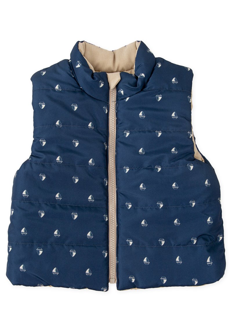 Chaleco acolchado de color azul marino con cremallera en la parte delantera, que presenta pequeños patrones de barcos. El interior tiene un forro color crema, con un cuello alto y textura acolchada.