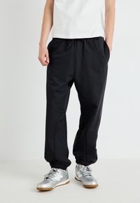Pantaloni de trening negri cu mansete elastice, buzunare laterale și un cordon la talie, fabricați dintr-un material moale, asortați cu încălțăminte sport argintie.