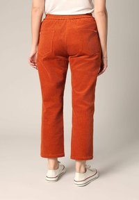 Gebrande oranjerode corduroy broek met een elastische tailleband, rechte pijpen en twee achterzakken, gecombineerd met witte sneakers.