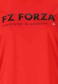 Röd T-shirt i mjukt tyg, med svart text "FZ FORZA" och "INNOVATED IN DENMARK," prydd med en liten dansk flagga.