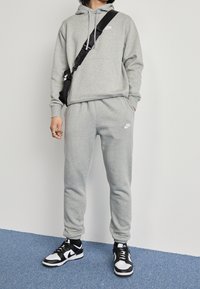 Grå hoodie och sweatpants gjorda av mjukt material med elastiska muddar; har små vita Nike-logotyper. Svart och vita sneakers kompletterar outfiten.