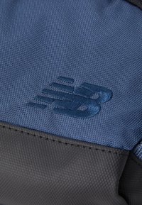 Borsa sportiva in tessuto blu e nero con superficie texturizzata e logo New Balance ricamato in blu abbinato. Cuciture visibili.