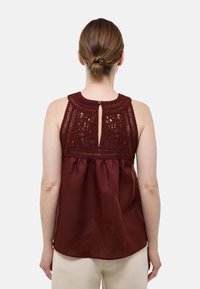 Top sans manches bordeaux avec un empiècement en dentelle au crochet et un détail de dos en forme de clé, présentant une coupe décontractée avec une taille froncée et une texture lisse.