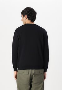Black sweatshirt with a relaxed fit, crew neck, ribbed cuffs, and hem. Paired with olive green cargo pants featuring back pockets.