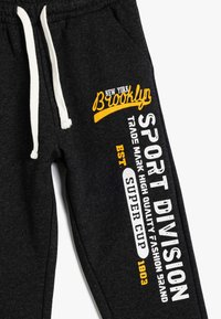 Ciemnoszare dresy z białym sznurkiem, z żółtym i białym nadrukiem tekstu "Brooklyn", "SPORT DIVISION" oraz "SUPER CUP 1903" na boku.