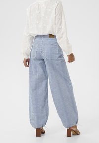 Pánské kalhoty s širokými nohavicemi, pruhované v modro-bílé kombinaci, s elastickým pasem a stahovacími manžetami na kotnících. Viditelné zadní kapsy.