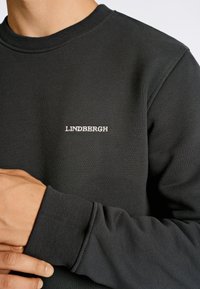 Sudadera negra hecha de una tela suave, con cuello redondo y puños acanalados. Pequeño logotipo "LINDØBERGH" bordado en el pecho.