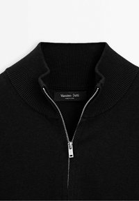 Pull en maille côtelée noire avec demi-fermeture éclair argentée et col montant, avec une étiquette "Massimo Dutti" à l'intérieur de l'encolure.