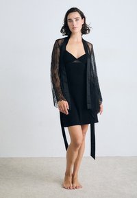 Juodas nėriniuotas kimono su ilgomis rankovėmis, dėvimas virš prigludusio juodo slipsukos. Lietaus tekstūra, satino apdaila ir sudėtingi nėriniai ant rankovių.
