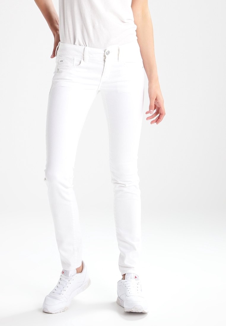 Jeans blancos ajustados fabricados en denim, con un diseño clásico de cinco bolsillos y cierre de botón metálico. Combinados con zapatillas blancas.