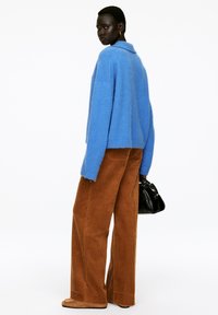 Blauer, flauschiger Pullover, weite braune Cordhosen und schwarze Handtasche. Strukturierter Stoff, oversized Passform und sichtbare Nahtdetails.