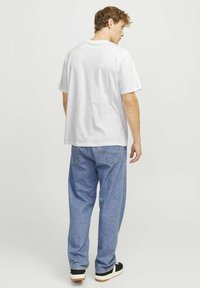 Bijela pamučna majica kratkih rukava u kombinaciji s laganim plavim trapericama slobodnog kroja. Outfit se odlikuje jednostavnim, ležernim dizajnom.