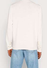 Pull beige clair à manches longues avec une texture en maille fine, col rond et poignets côtelés, porté avec un jean en denim bleu clair.