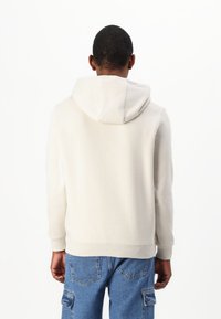 Sudadera de color beige claro con una textura suave, que cuenta con capucha con cordón y puños de canalé. Combinada con unos vaqueros cargo azules.